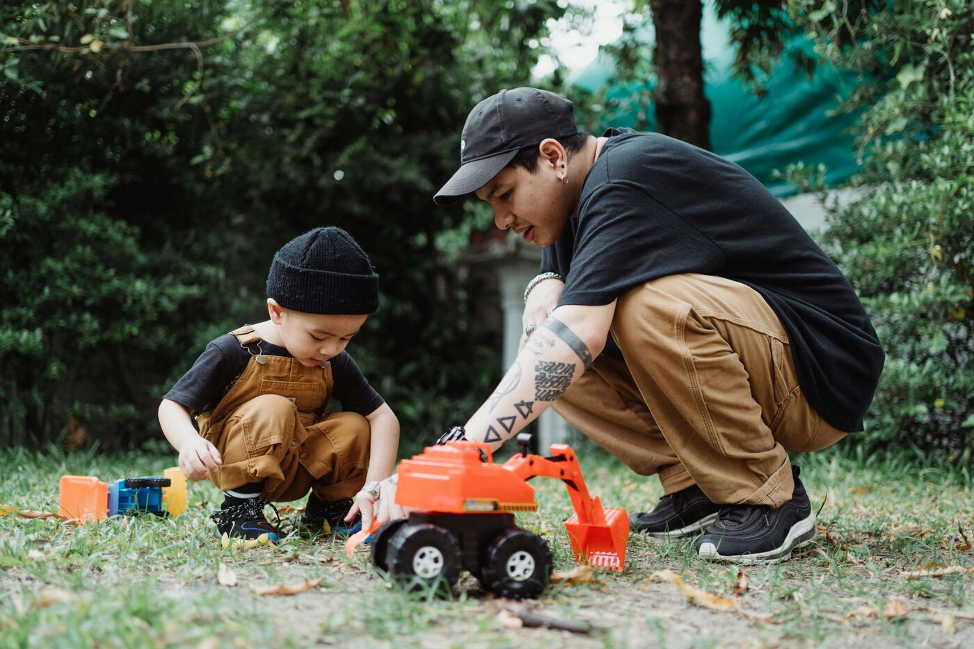 A parent and child play with toy trucks outdoors