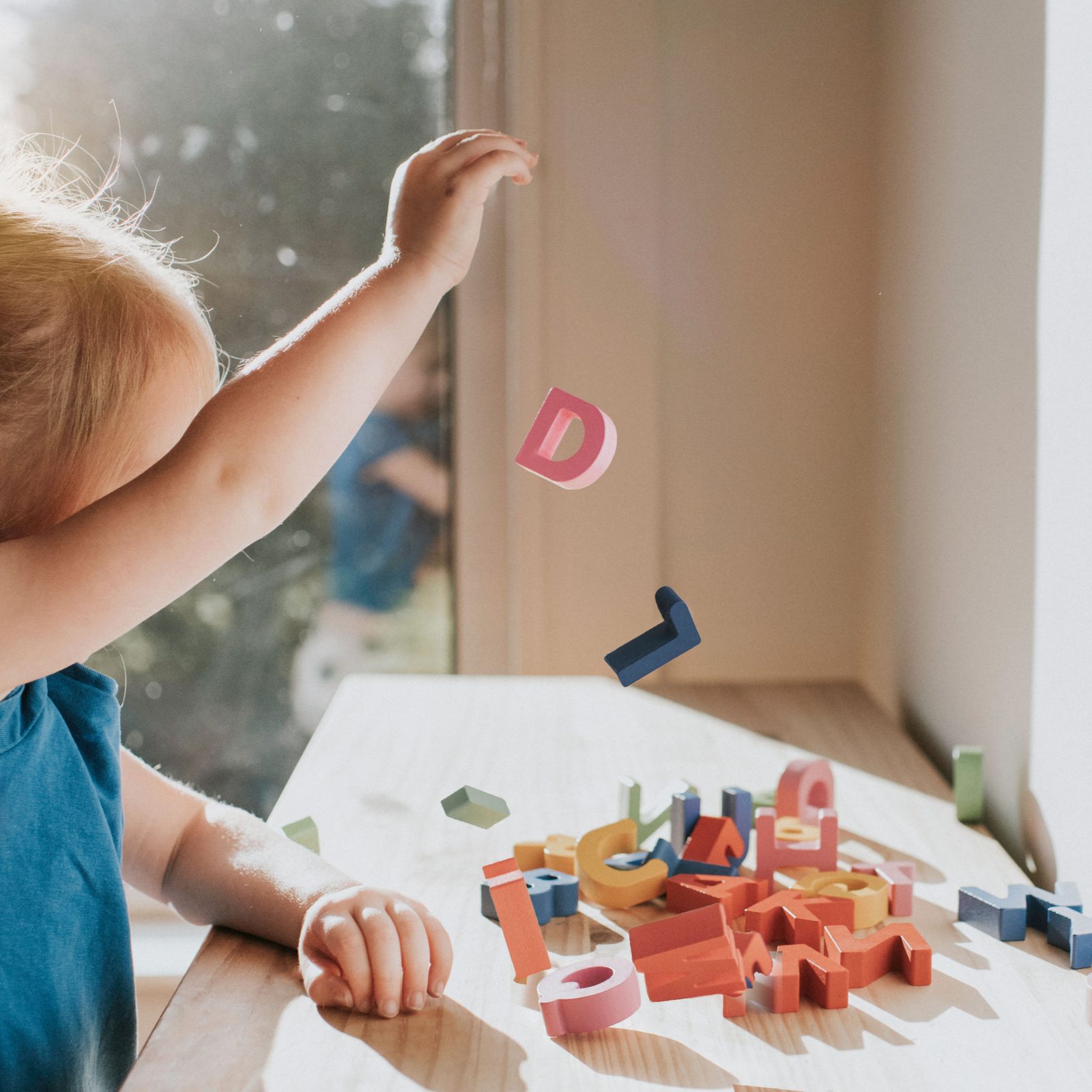 Child tossing magnetic letters at a sunlit table